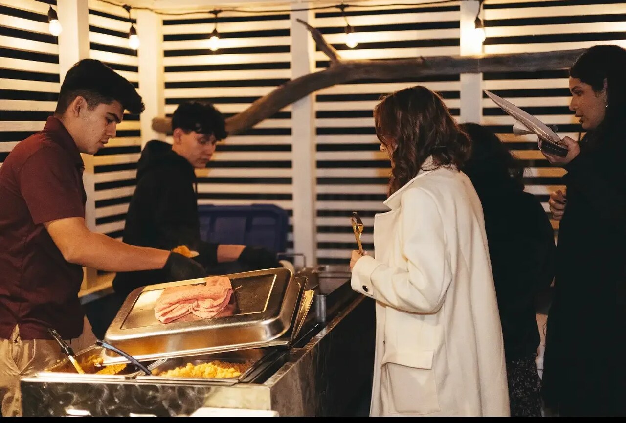 A B&C Burgers cook serving a guest from the cart at an evening event, under string lights