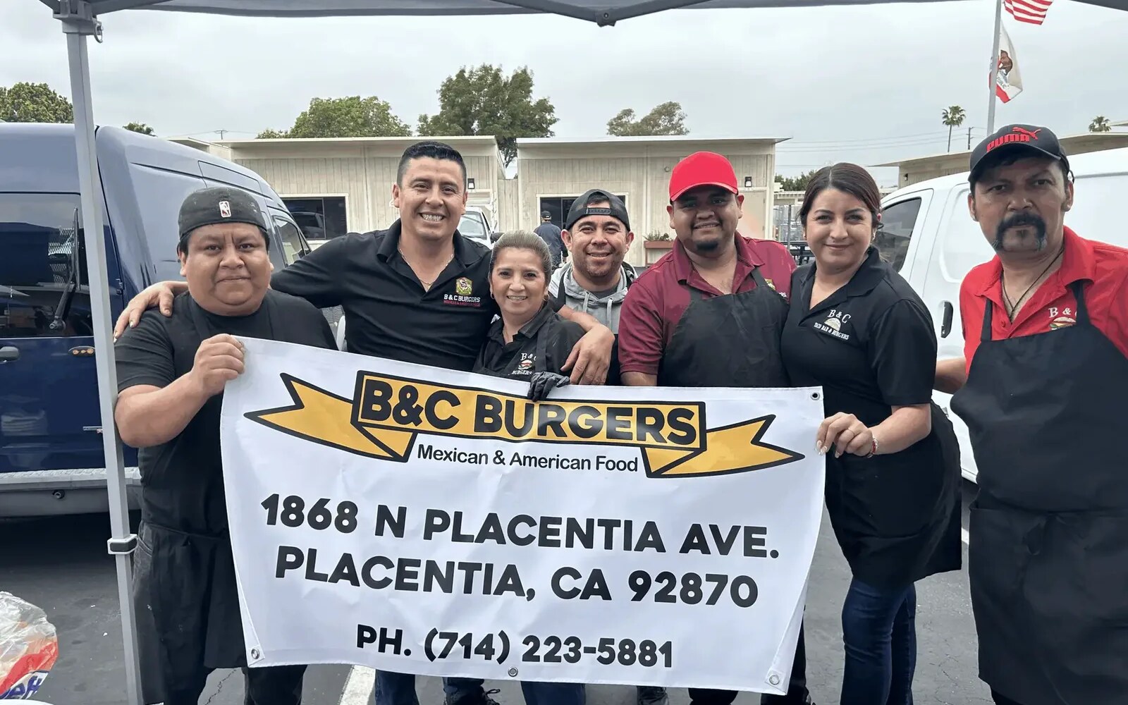 The B&C Burgers crew at a catering job, holding a banner with the restaurant’s address and phone number